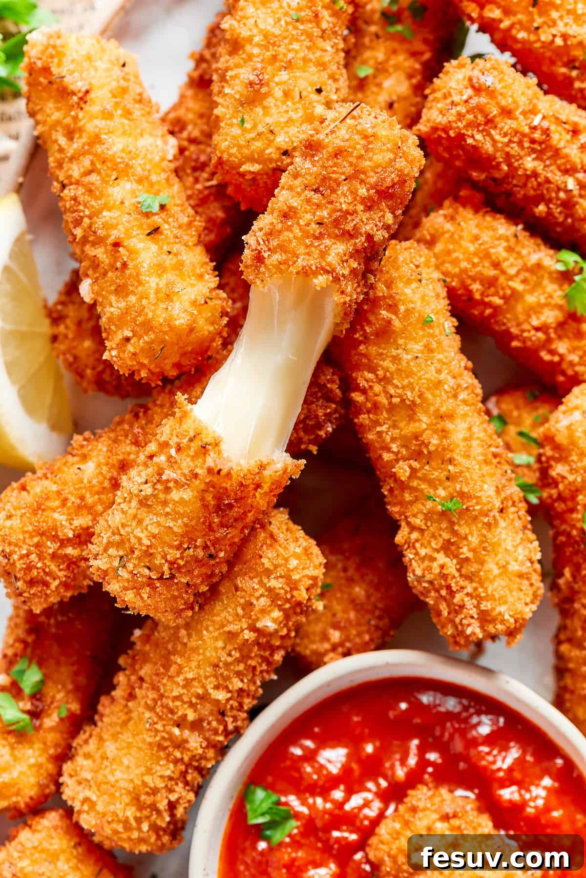 A freshly fried mozzarella stick is broken open to reveal the perfectly melted, stretchy mozzarella cheese inside, highlighting its gooey texture.
