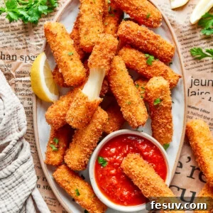 A platter of mozzarella sticks with one cut in half and one dipped in tomato sauce.