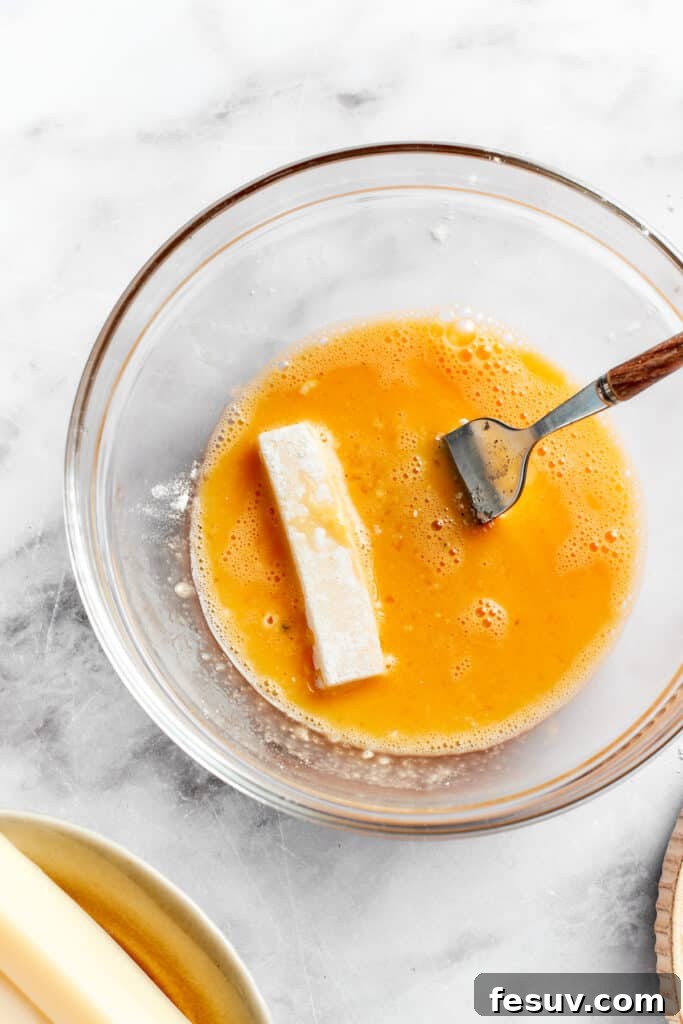 A mozzarella stick being carefully dipped into a bowl of beaten egg as part of the breading process.