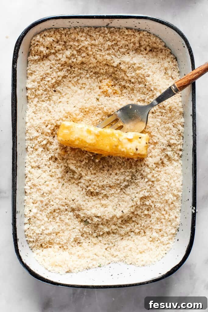 A mozzarella stick, fully coated in panko breadcrumbs, rests in a dish, ready for freezing.