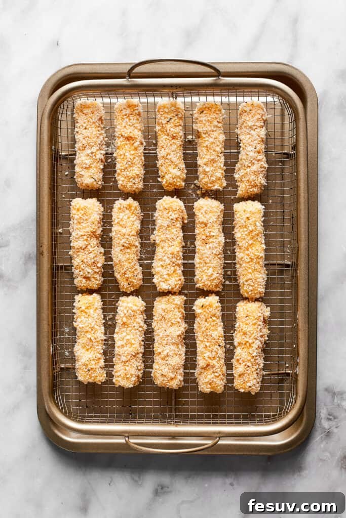 A rack filled with perfectly breaded mozzarella sticks, arranged in a single layer, ready for the freezer.