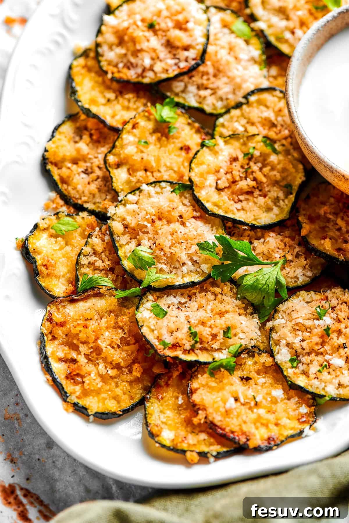 A beautifully arranged pile of golden-brown zucchini chips on a pristine white plate, garnished with fresh herbs, ready to be enjoyed.