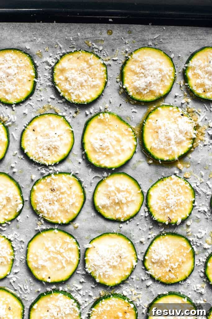 Zucchini slices on a baking sheet, evenly coated with the Panko and Parmesan breadcrumb mixture, ready for baking.