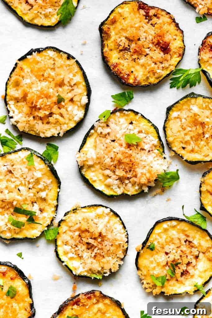 Perfectly baked, golden-brown zucchini chips are neatly arranged on a light-colored surface, showcasing their crispy texture.