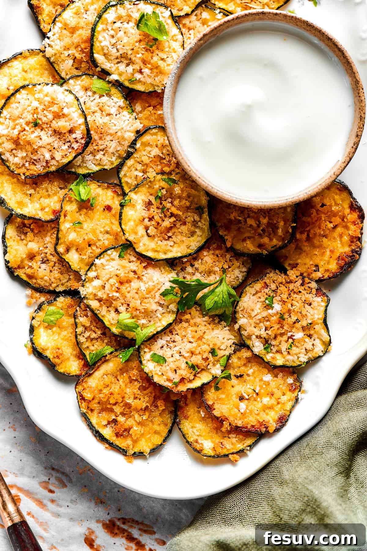 A rustic wooden platter piled high with golden, crispy zucchini chips, ready to be served and enjoyed as a savory snack.