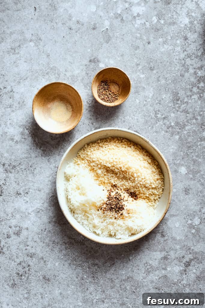 Separate bowls hold Panko breadcrumbs mixed with Parmesan, and individual seasonings like garlic powder and pepper.