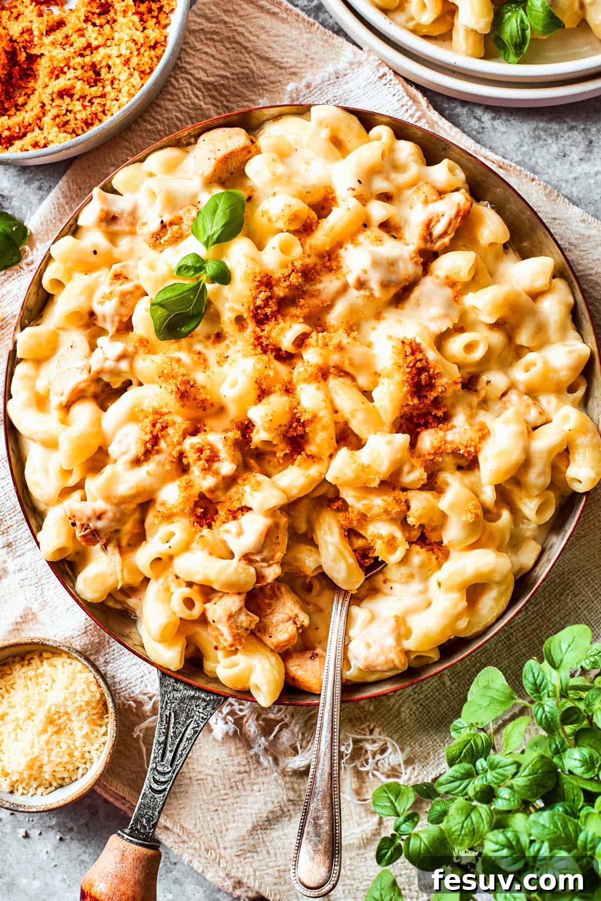 A skillet filled with creamy Chicken Mac and Cheese, being stirred with a spoon, highlighting the rich texture and visible chicken pieces.