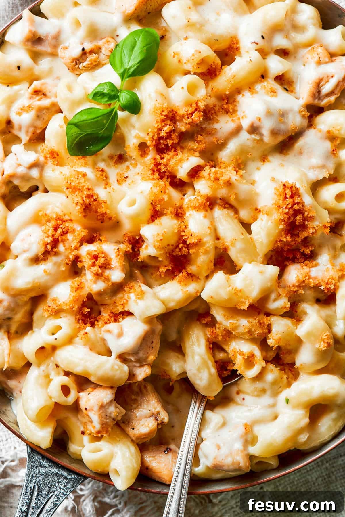 A close-up view of a bowl of rich, creamy Chicken Mac and Cheese, with a spoon stirring through the gooey pasta and chicken, ready to be enjoyed.