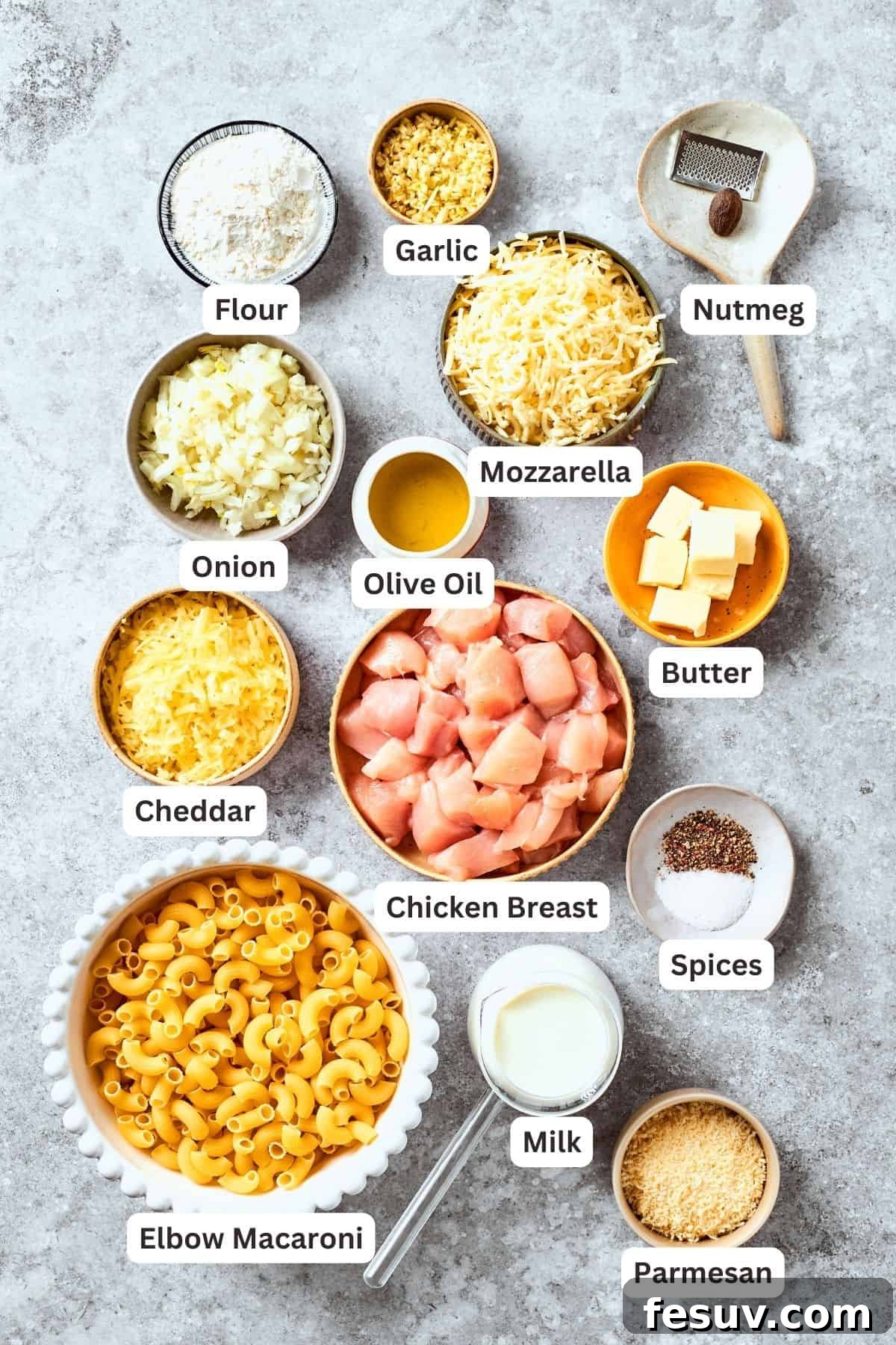 All the fresh ingredients for Chicken Mac and Cheese are neatly portioned and labeled on a wooden surface: macaroni, chicken breast, onion, garlic, olive oil, flour, salt, pepper, spices, cheddar, mozzarella, Parmesan cheese, and milk.