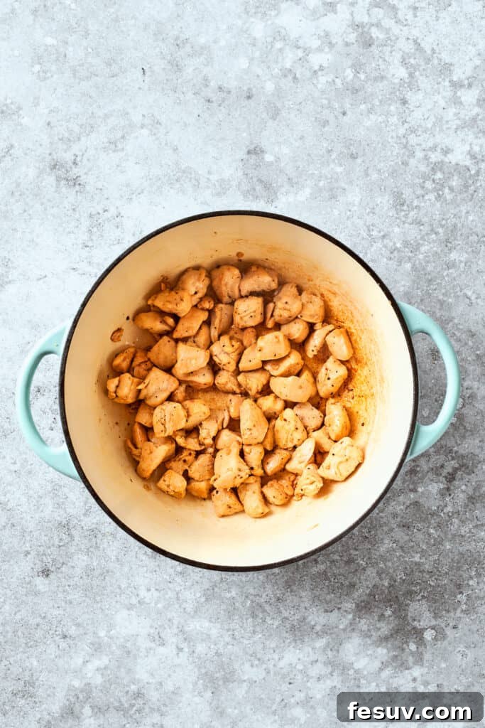 Bite-sized chicken pieces are cooking in a skillet, turning golden brown.