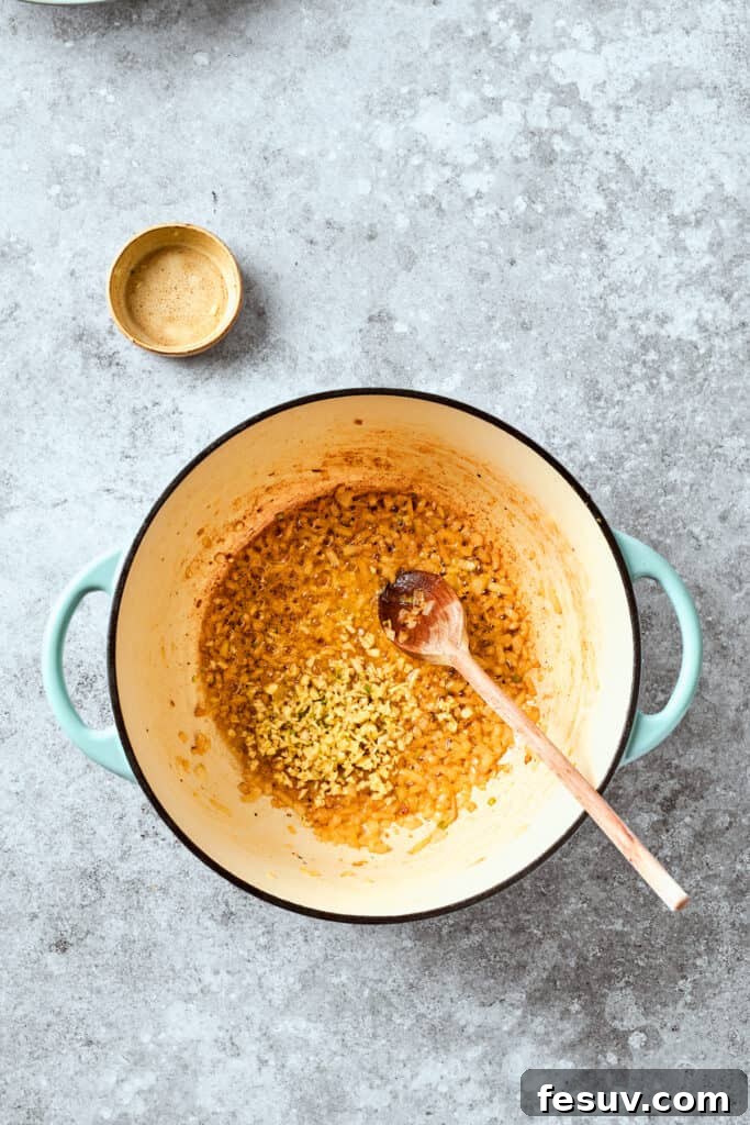 Minced garlic cloves are being added to the softened onions in a skillet, creating an aromatic foundation for the cheese sauce.