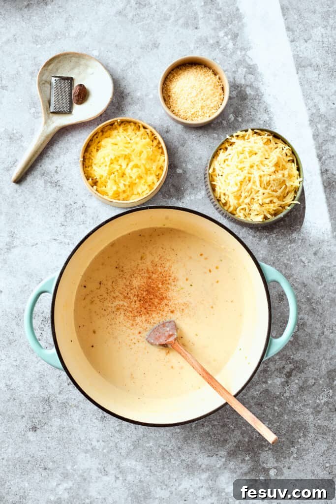 A pinch of nutmeg is being stirred into the golden-brown roux in a skillet, infusing the sauce with warm spice.