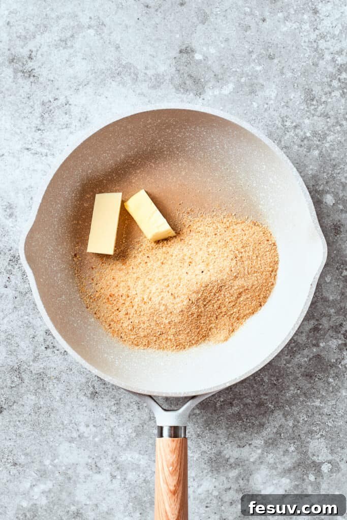 Melted butter is added to Panko breadcrumbs in a pan, preparing them for a golden, crunchy topping.