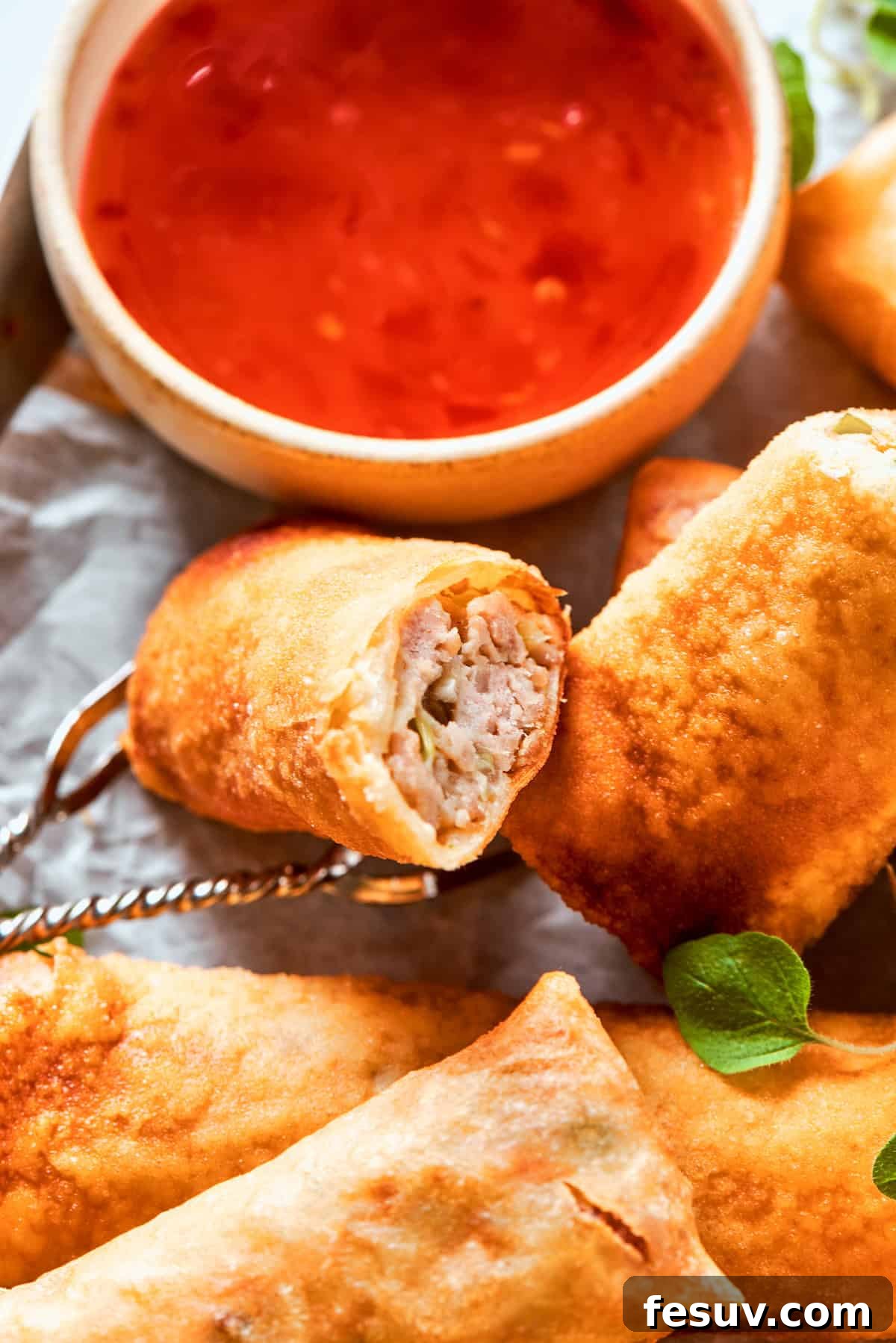 A stunning plate of perfectly golden and crispy chicken egg rolls, served alongside a vibrant bowl of red sweet chili sauce, ready for dipping and enjoying.