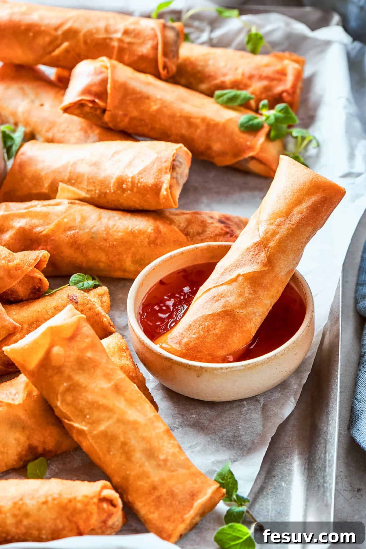 A close-up of a crispy chicken egg roll being dipped into a small bowl of savory sauce, with more golden egg rolls scattered on a serving surface around it, highlighting the delicious interaction.