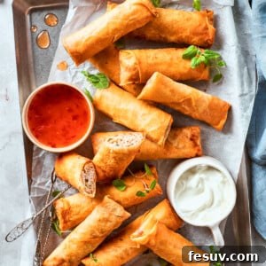 A bowl of red sauce and a bowl of white sauce are served on a serving tray full of chicken egg rolls.