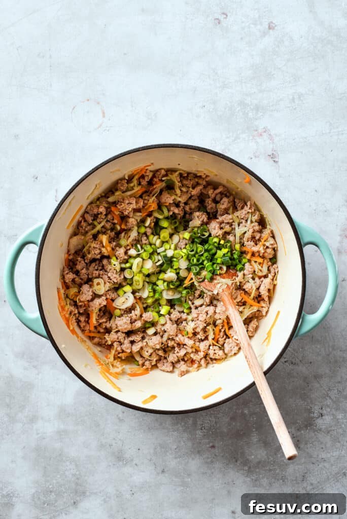 Fresh green onions being stirred into the cooked chicken and vegetable filling, adding a final touch of freshness and flavor.
