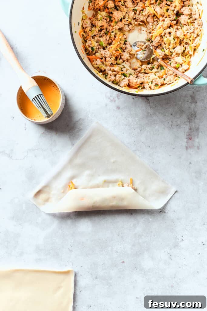 The first fold of the egg roll wrapper, bringing the bottom corner over the filling, demonstrating proper wrapping technique.