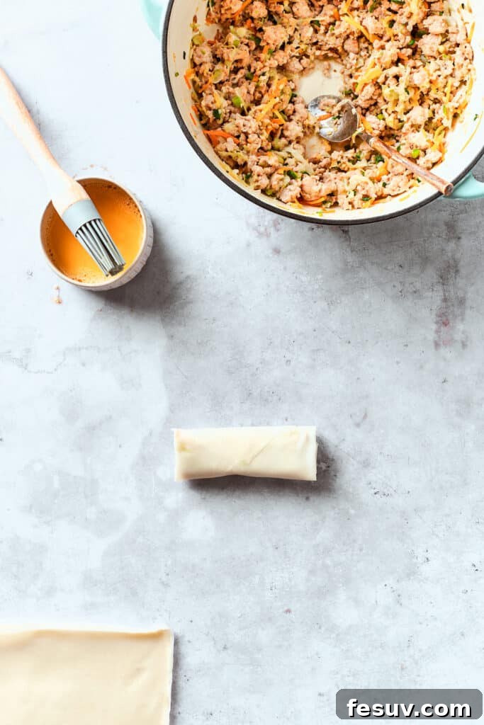 A close-up of an egg roll being brushed with a beaten egg wash, a crucial step for achieving a golden and crispy seal during frying.