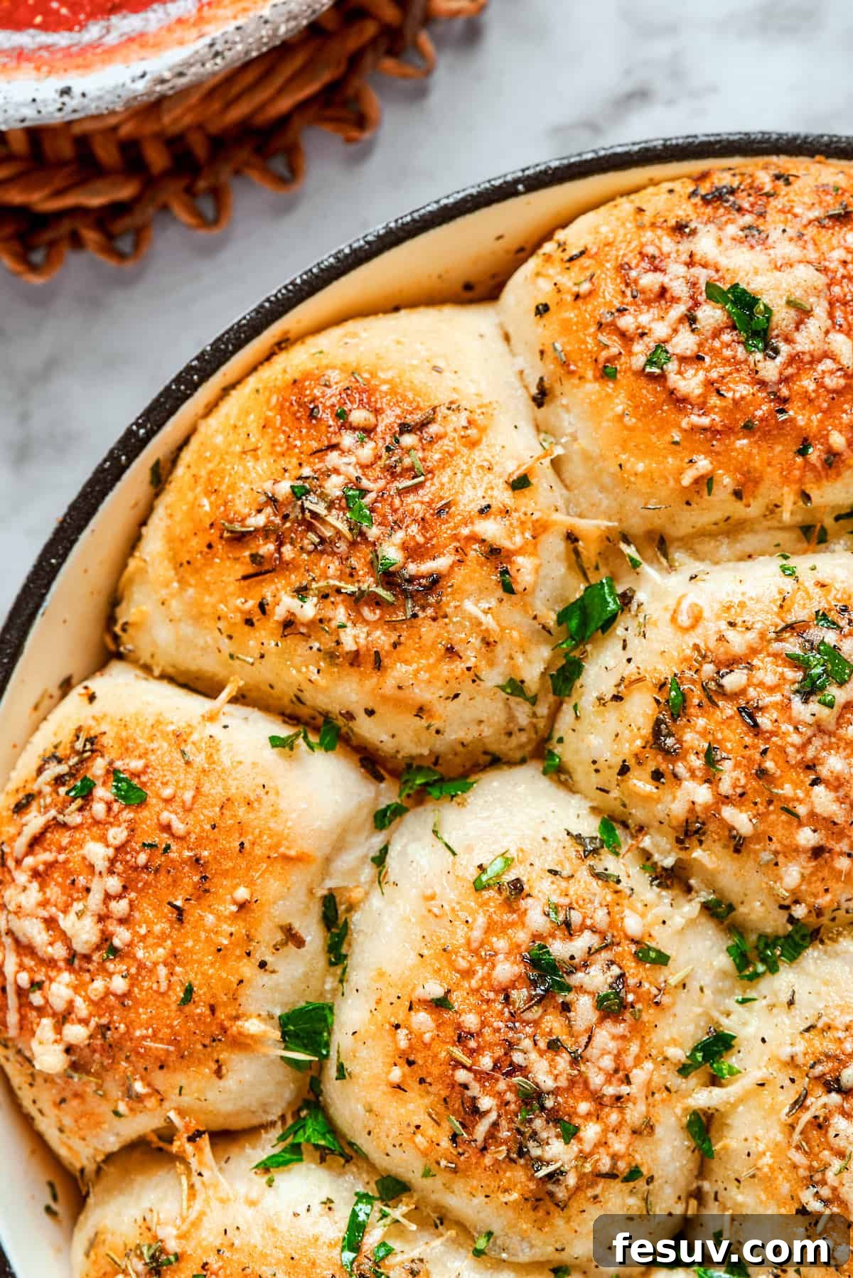 This easy Pizza Bites recipe stuffs spicy pepperoni and gooey mozzarella cheese into little pieces of pizza dough brushed with herb butter. A cast iron skillet filled with freshly baked pizza bites, garnished generously with vibrant green herbs like parsley, showcasing their golden crust.