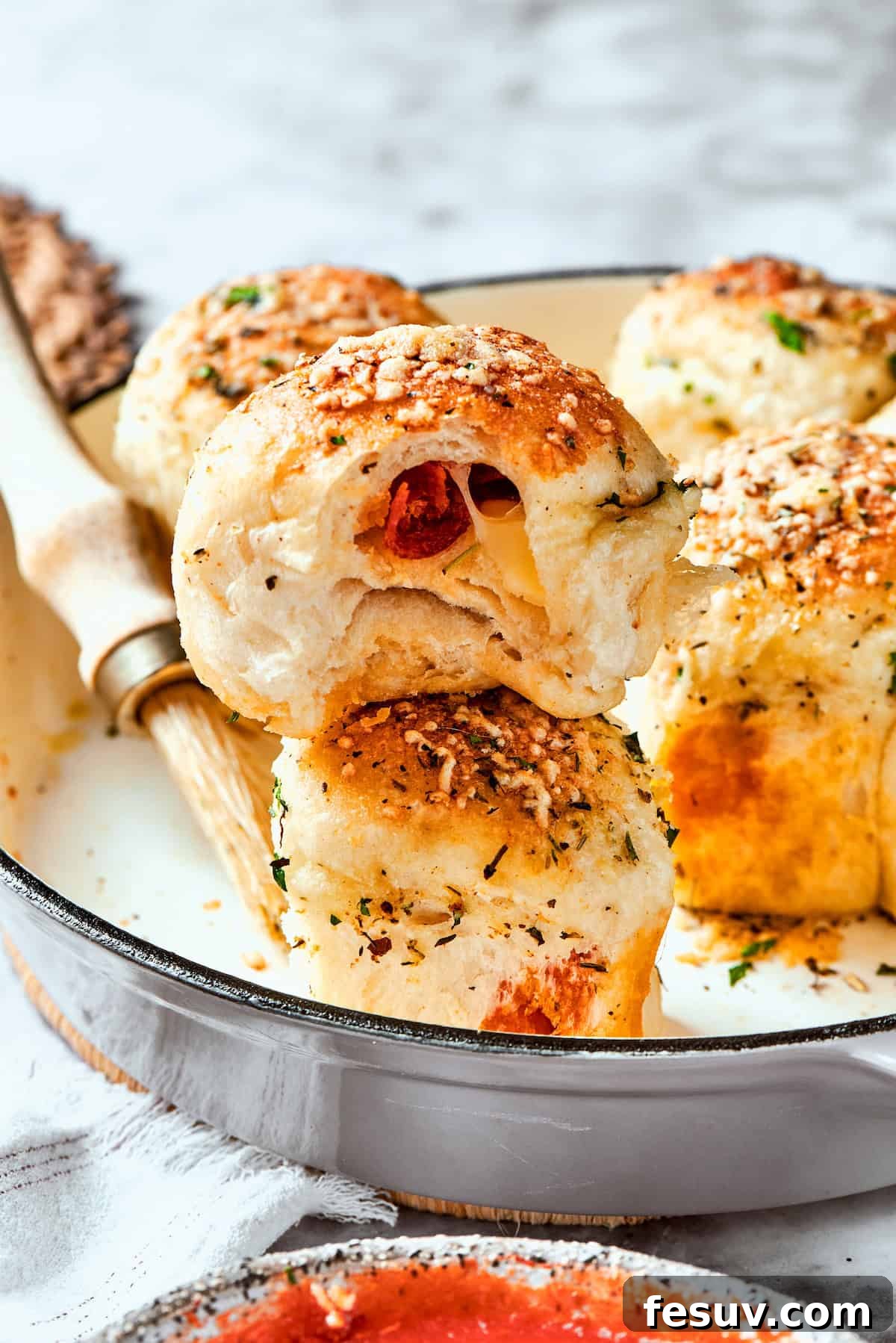 This easy Pizza Bites recipe stuffs spicy pepperoni and gooey mozzarella cheese into little pieces of pizza dough brushed with herb butter. A serving utensil delicately lifts a single pizza bite from a skillet, showcasing its perfectly golden exterior and inviting texture, with the rest of the bites in the background.