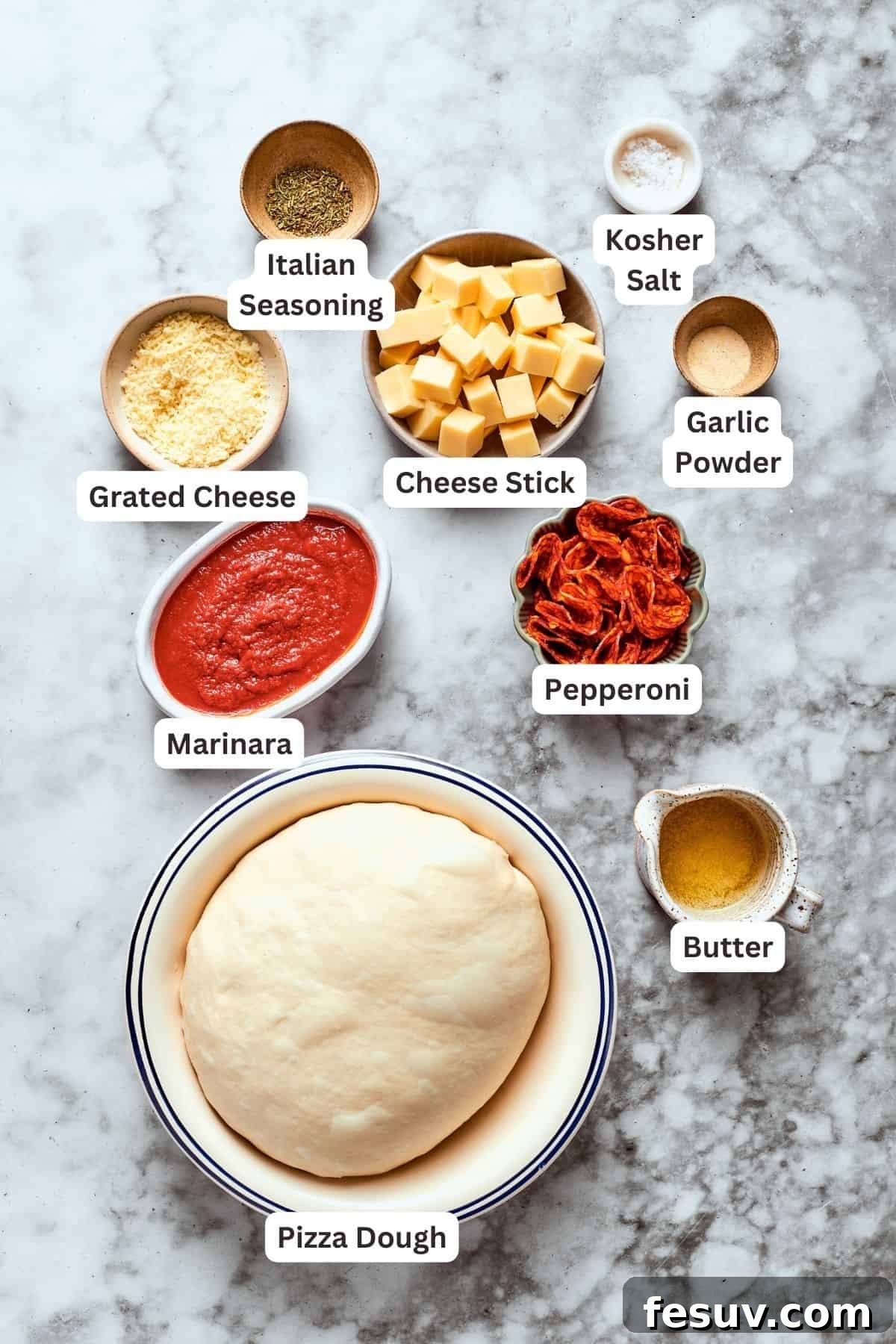 This easy Pizza Bites recipe stuffs spicy pepperoni and gooey mozzarella cheese into little pieces of pizza dough brushed with herb butter. Neatly arranged ingredients for pizza bites: pizza dough, shredded cheese, Italian seasoning, marinara sauce, pepperoni slices, melted butter, garlic powder, a cheese stick, and salt.