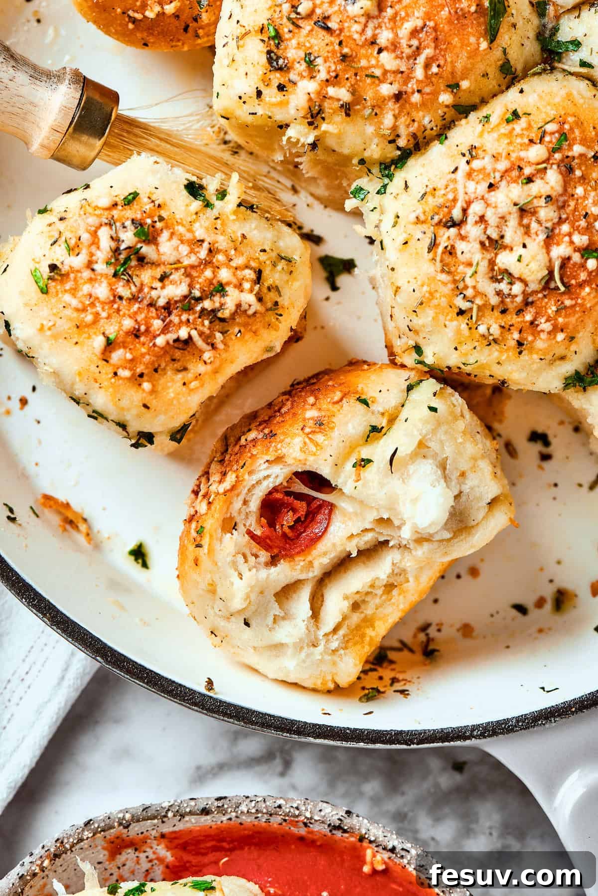 This easy Pizza Bites recipe stuffs spicy pepperoni and gooey mozzarella cheese into little pieces of pizza dough brushed with herb butter. A few freshly baked pizza bites are shown artfully arranged in a cast iron skillet, ready to be served.