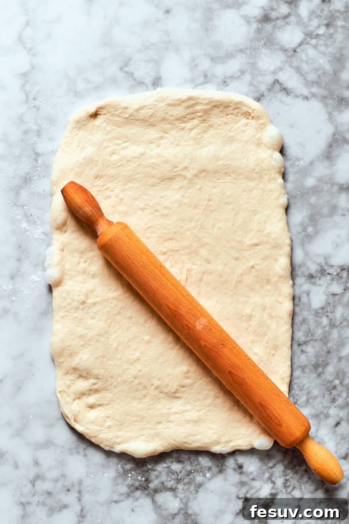 This easy Pizza Bites recipe stuffs spicy pepperoni and gooey mozzarella cheese into little pieces of pizza dough brushed with herb butter. Pizza dough being rolled out evenly with a rolling pin on a floured surface.