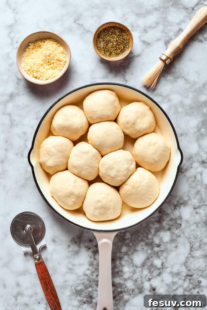 This easy Pizza Bites recipe stuffs spicy pepperoni and gooey mozzarella cheese into little pieces of pizza dough brushed with herb butter. All 12 prepared pizza bites are neatly arranged with seams down in a greased cast iron skillet, ready for baking.