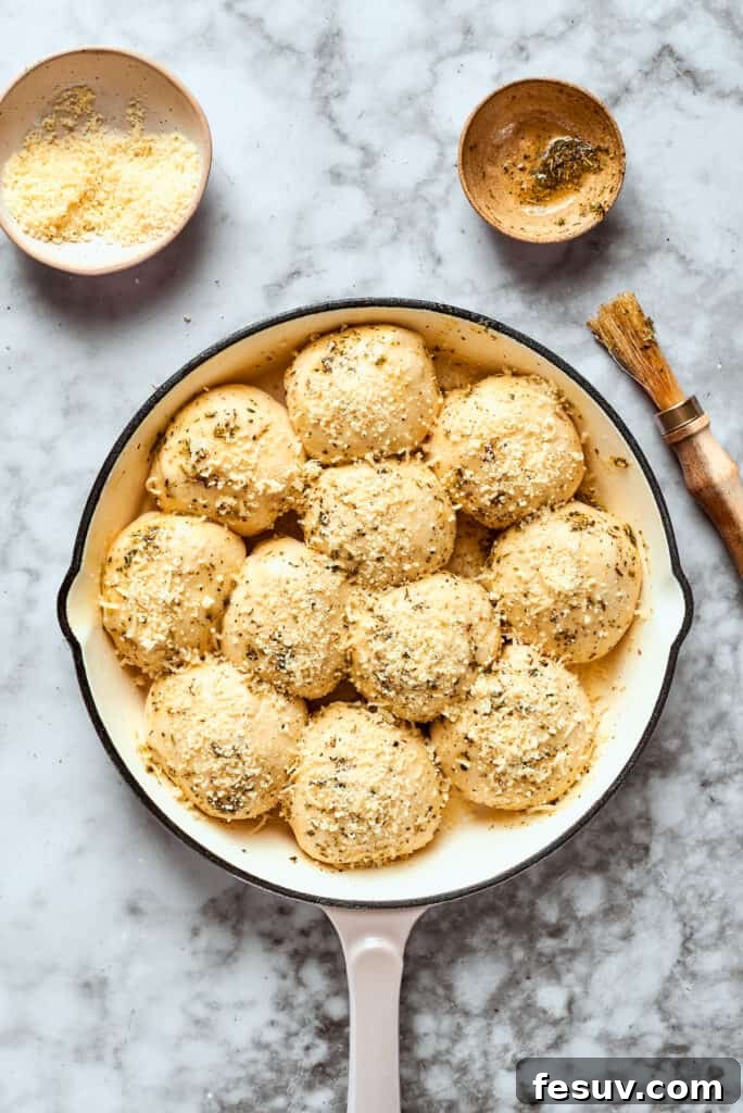 This easy Pizza Bites recipe stuffs spicy pepperoni and gooey mozzarella cheese into little pieces of pizza dough brushed with herb butter. The pizza bites in the skillet are brushed with herb butter and sprinkled with grated cheese, appearing prepped and ready for the oven.