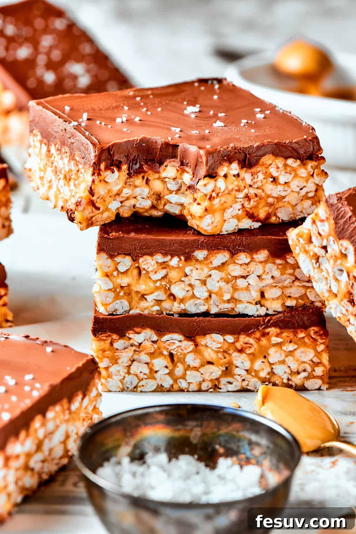 No-bake Peanut Butter Rice Crispy Treats are swirled with creamy peanut butter and capped with a rich layer of melted milk chocolate. A stack of golden brown peanut butter rice crispy treats, with the top bar showing a delicious bite taken out of it, revealing the chewy interior and rich chocolate topping.
