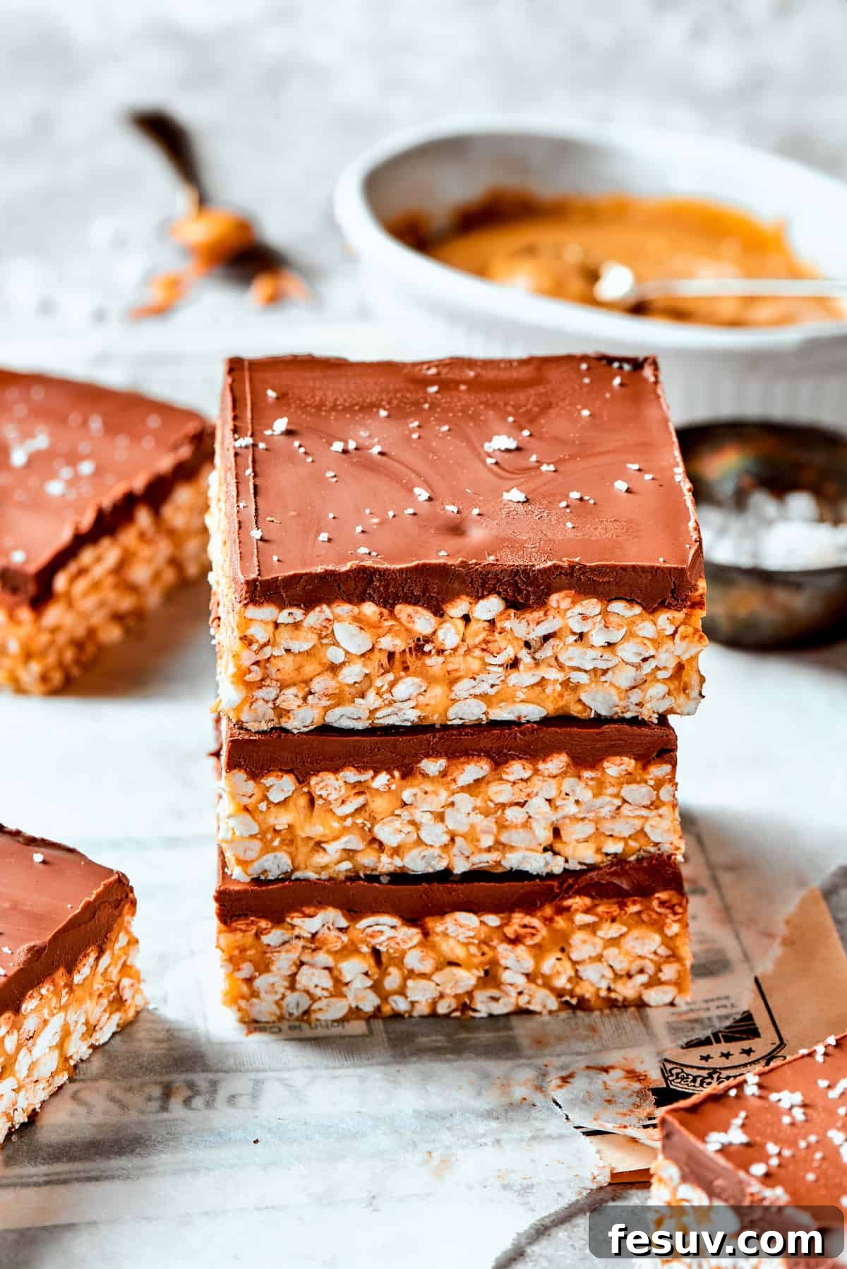 No-bake Peanut Butter Rice Crispy Treats are swirled with creamy peanut butter and capped with a rich layer of melted milk chocolate. Three golden brown crispy rice bars, generously topped with a rich layer of melted milk chocolate, are stacked appealingly one on top of the other.