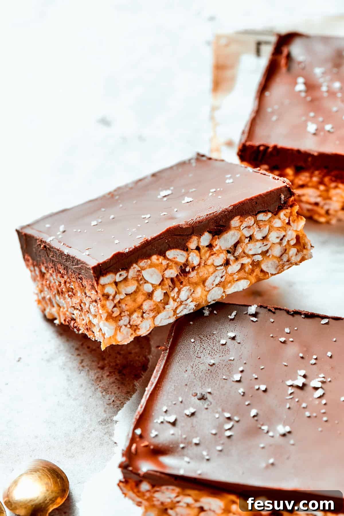 No-bake Peanut Butter Rice Crispy Treats are swirled with creamy peanut butter and capped with a rich layer of melted milk chocolate. A perfectly square bar of peanut butter rice krispies is shown up close, glistening with a smooth layer of melted milk chocolate on top.
