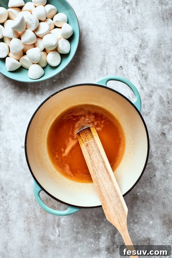 No-bake Peanut Butter Rice Crispy Treats are swirled with creamy peanut butter and capped with a rich layer of melted milk chocolate. A spoon stirs the melting butter and maple syrup in a saucepan on the stove.