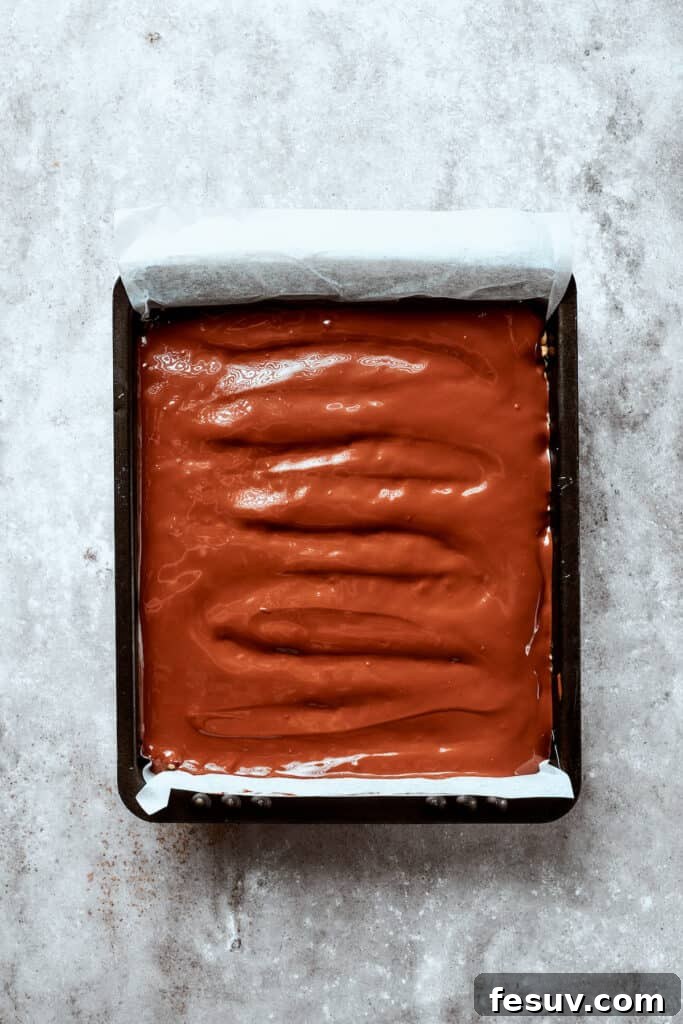 No-bake Peanut Butter Rice Crispy Treats are swirled with creamy peanut butter and capped with a rich layer of melted milk chocolate. A generous, smooth layer of melted milk chocolate is poured over the pressed peanut butter rice crispy base in the baking dish.