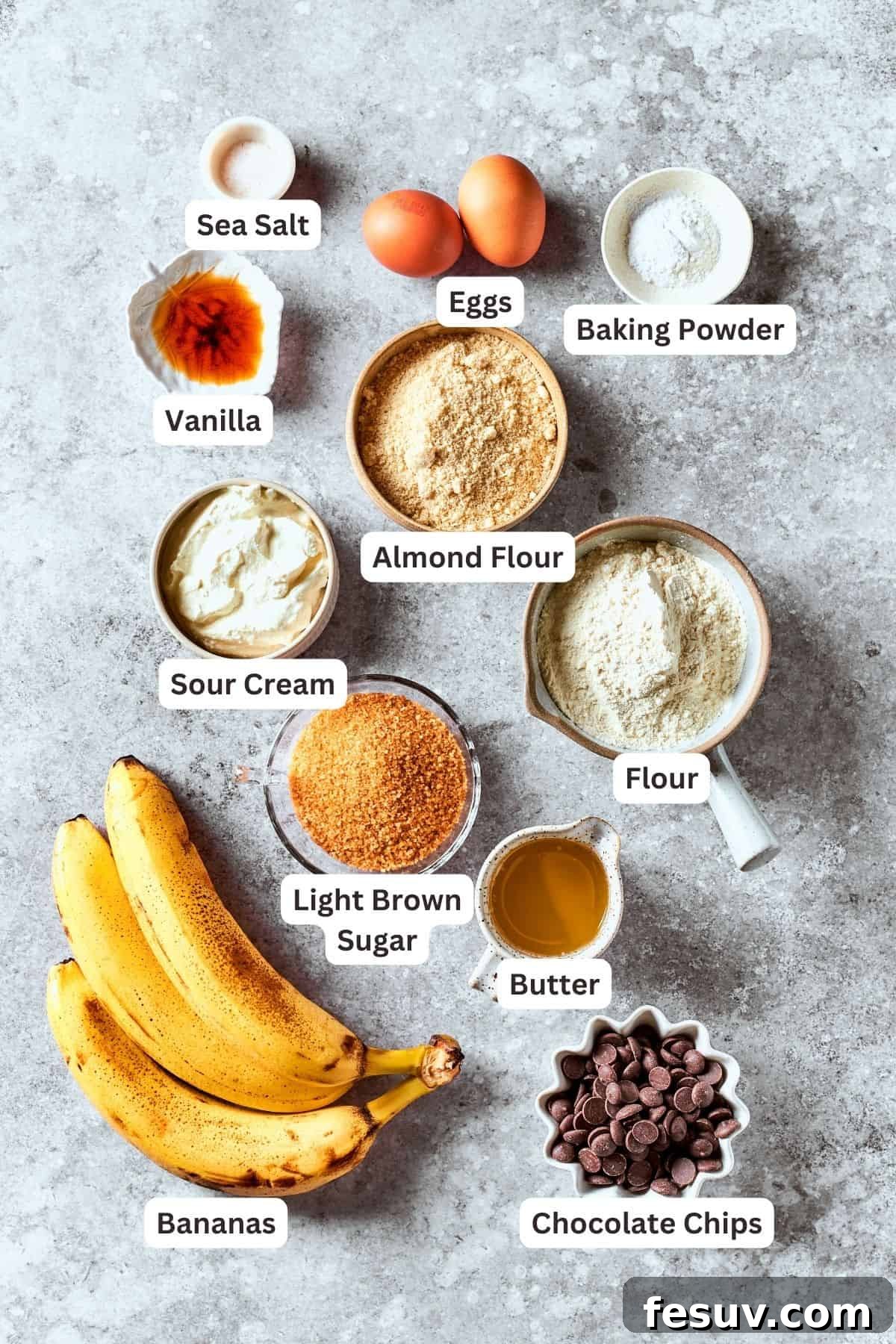 Ingredients for homemade sour cream banana bread are labelled and portioned out: ripe bananas, brown sugar, almond flour, sour cream, all-purpose flour, baking powder, eggs, vanilla extract, salt, chocolate chips, and melted butter.