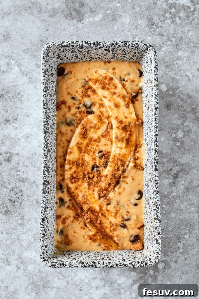 Banana bread batter in a loaf pan, topped with elegant banana slices before baking.