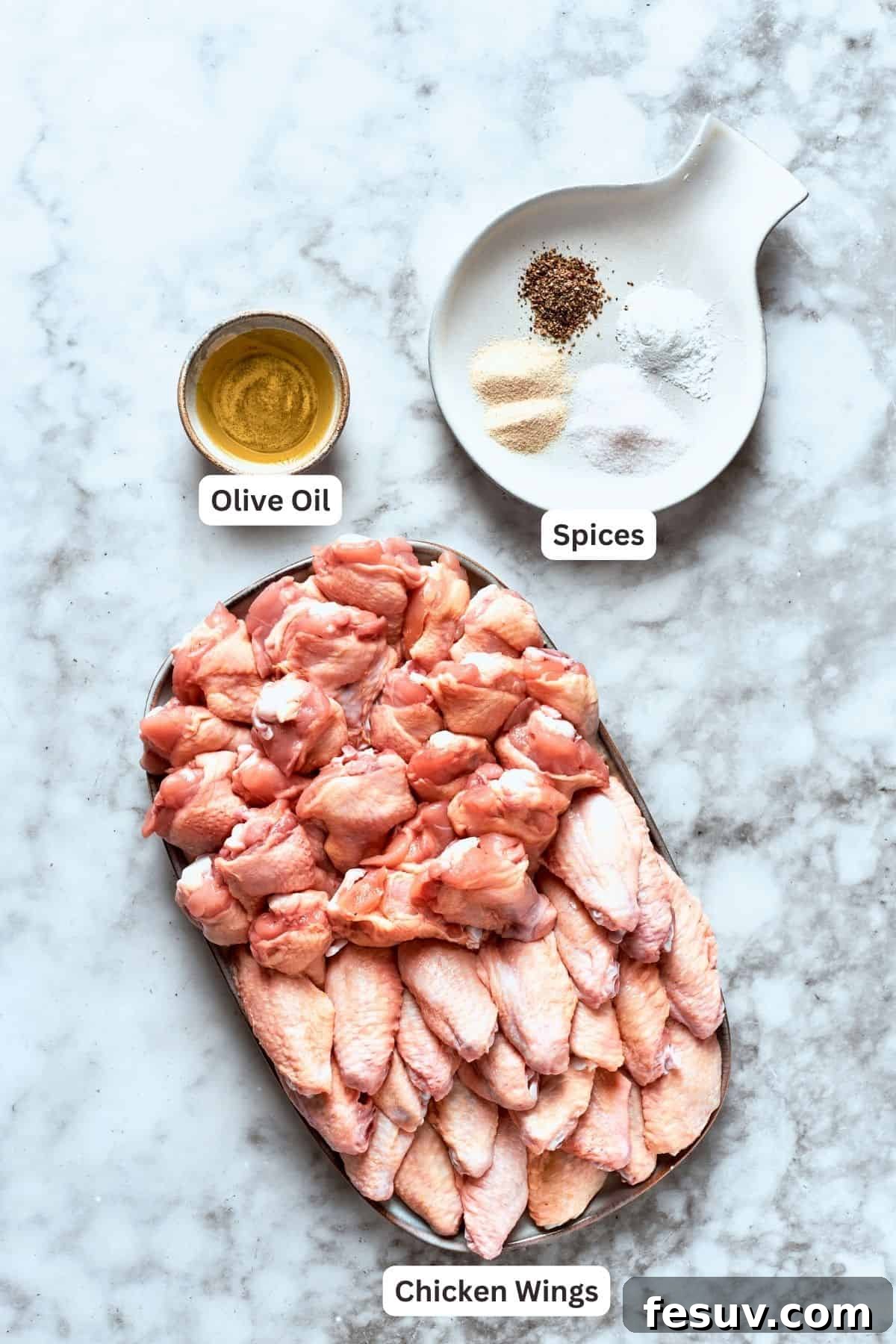 This easy Buffalo Wings recipe soaks crisp fried wings in a homemade buffalo sauce that's loaded with hot sauce and honey for intense flavor. Ingredients for buffalo wings are labeled and portioned: chicken, olive oil, spices, baking powder.