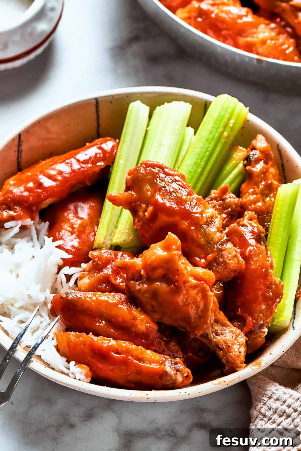 This easy Buffalo Wings recipe soaks crisp fried wings in a homemade buffalo sauce that's loaded with hot sauce and honey for intense flavor. Buffalo chicken wings served in a bowl with celery sticks and rice.