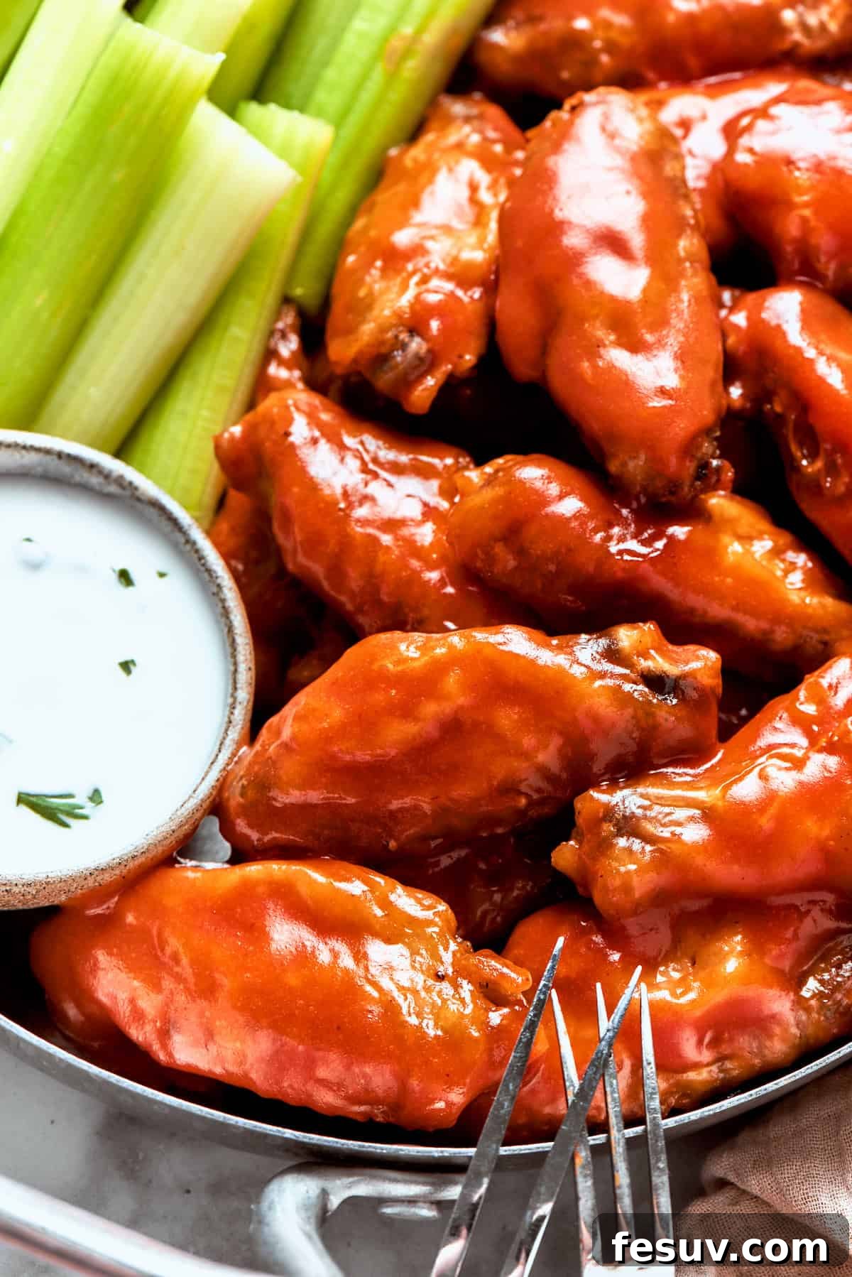 This easy Buffalo Wings recipe soaks crisp fried wings in a homemade buffalo sauce that's loaded with hot sauce and honey for intense flavor. Buffalo wings in a dish with dipping sauce and celery.