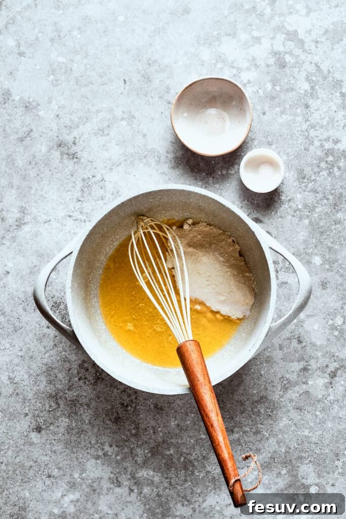 Starting the gravy with a classic butter and flour roux. Flour being whisked into melted butter in a saucepan to create a roux.