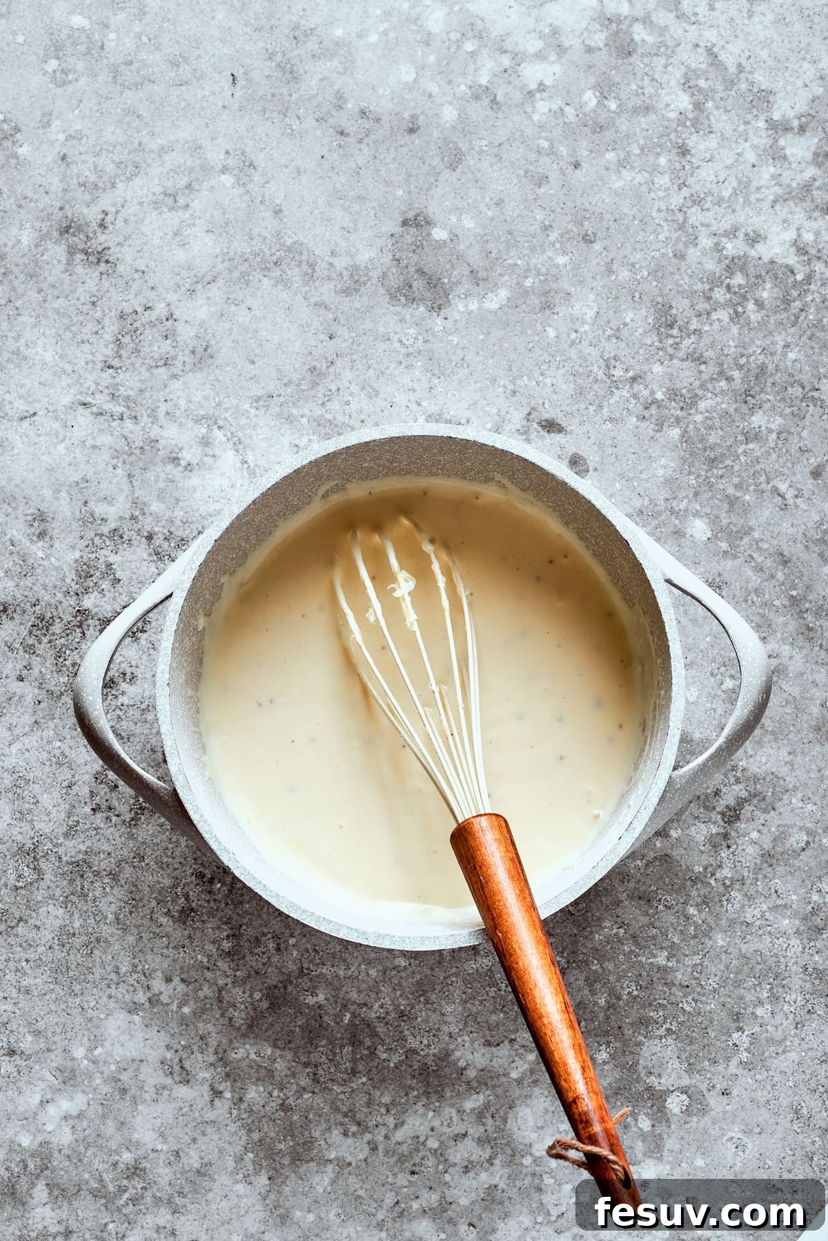 Whisking the gravy to a silky smooth consistency. A whisk blending the creamy gravy in a bowl until smooth and thickened.