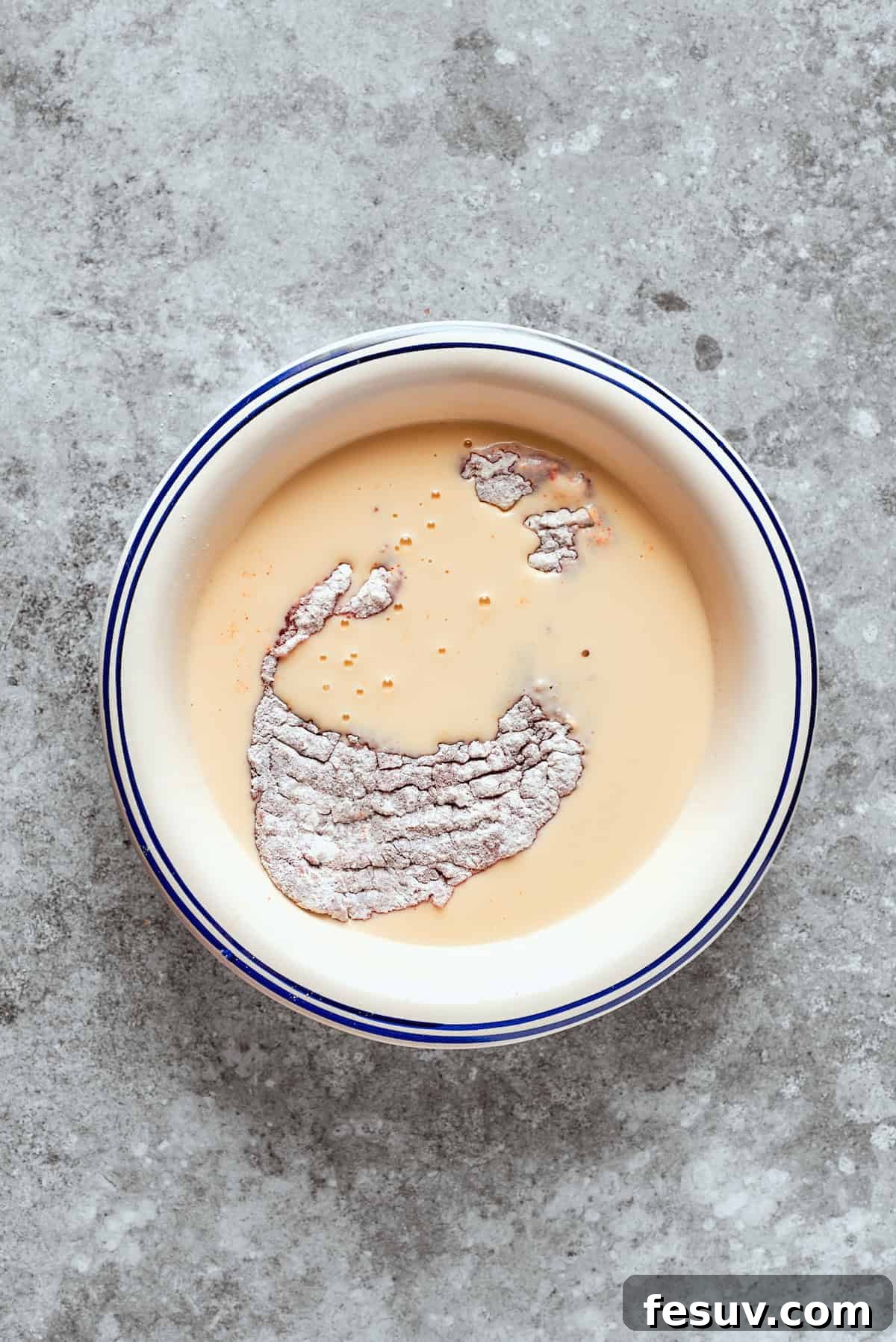 Dipping the steak into the buttermilk and egg mixture. The flour-dredged steak is placed into the beaten egg and buttermilk mixture.