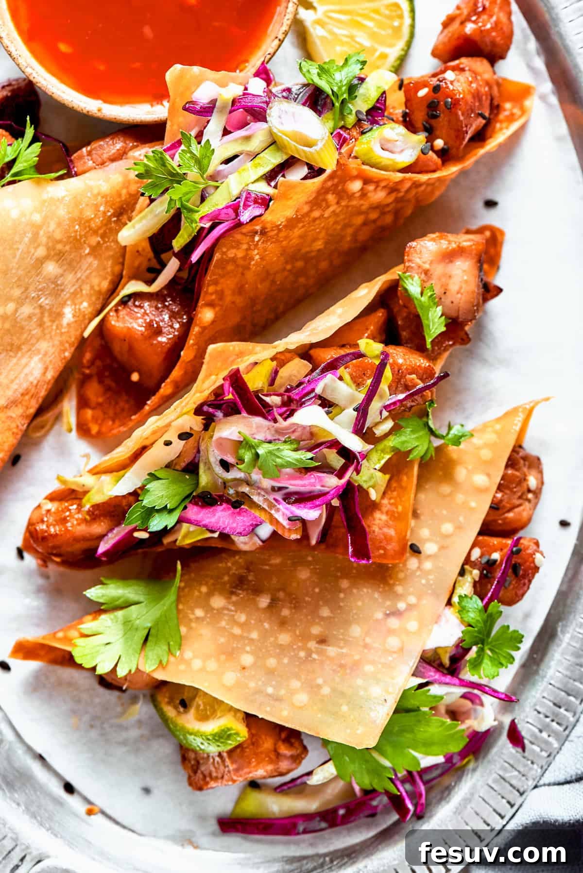 These Chicken Wonton Tacos feature bites of garlicky honey chicken stuffed into crisp wonton shells along with tangy fresh coleslaw. Overhead image of wonton tacos stuffed with cooked chicken and coleslaw.