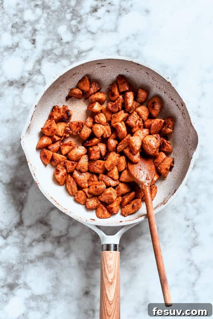 These Chicken Wonton Tacos feature bites of garlicky honey chicken stuffed into crisp wonton shells along with tangy fresh coleslaw. A spoon stirs the chicken as it browns and cooks in the skillet.