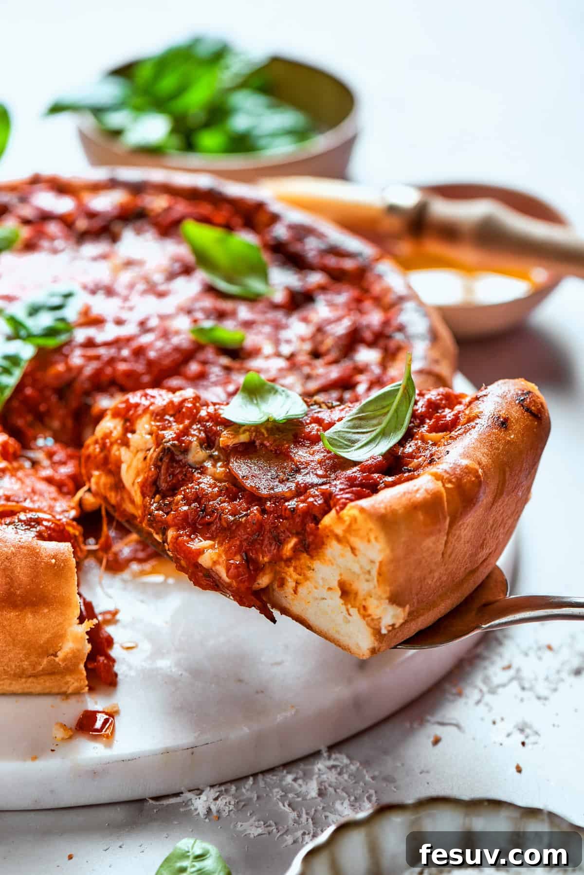 This Deep Dish Pizza features a buttery homemade crust, thick tomato sauce, and a blend of melted cheese plus pepperoni. A serving spoon lifts a decadent slice of deep dish pizza, showcasing its thick layers of cheese, sauce, and pepperoni, promising a rich and satisfying meal.