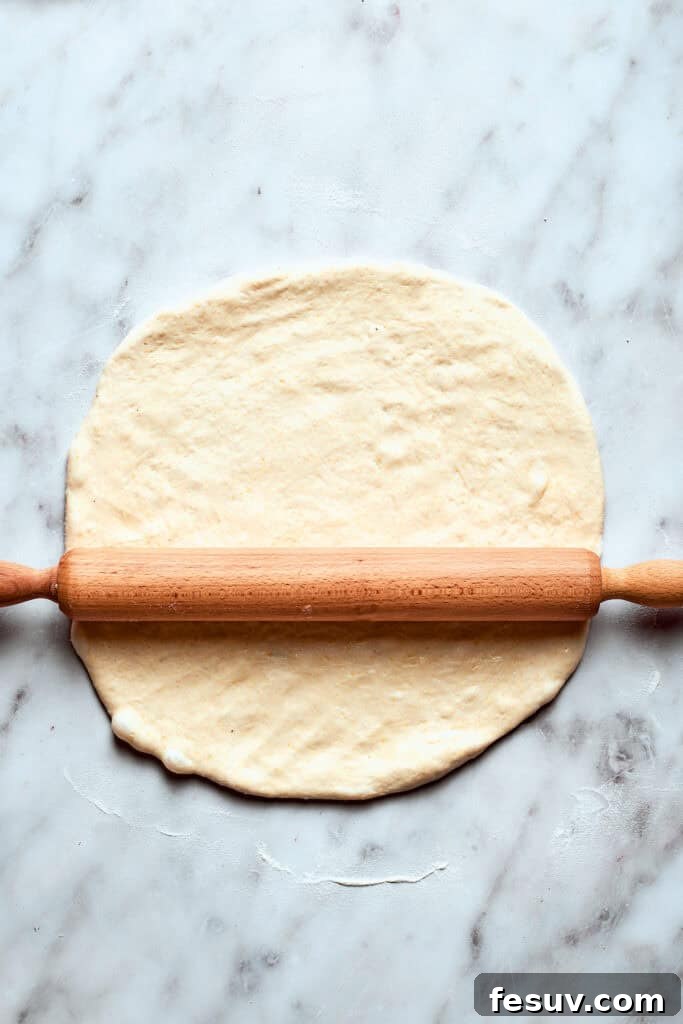 Roll out the deep dish pizza dough to fit your pan. A rolling pin expertly flattens a portion of deep dish pizza dough on a lightly floured surface, preparing it to be fitted into the pan.