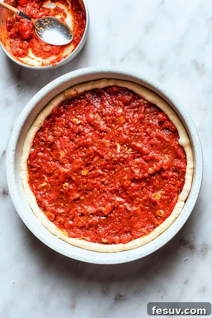 Pour the thick tomato sauce over the cheese layer. The rich, thick tomato sauce for deep dish pizza is carefully spread over the melted cheese layer in the pan, maintaining the unique Chicago layering.