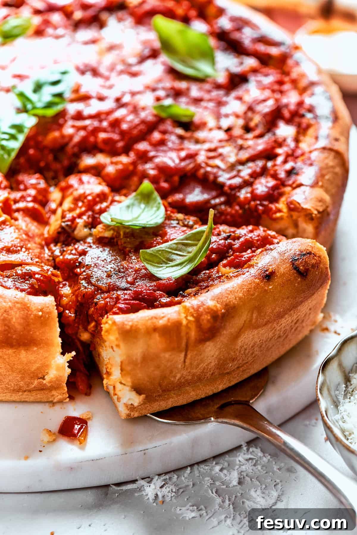 Serving a delicious slice of homemade Deep Dish Pizza. A hand holds a serving spoon, carefully lifting a generous slice of deep dish pizza out of the pan, revealing its gooey cheese, thick layers, and perfectly baked crust.