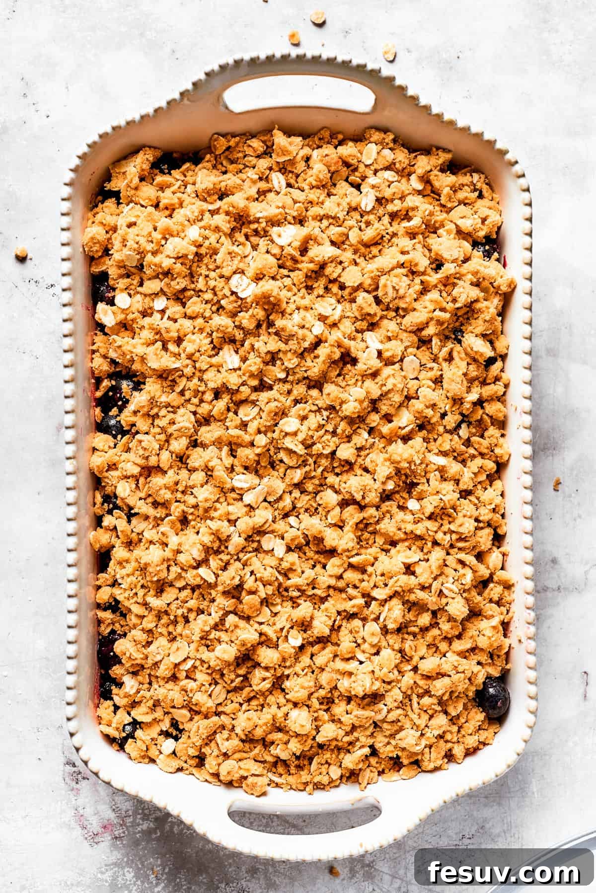 Topping the blueberries with the crisp crumble The buttery oat crumble topping is generously sprinkled over the blueberry filling in the baking dish, completely covering the berries.